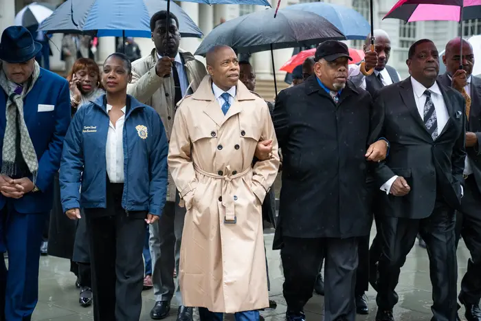 Mayor Eric Adams, wearing a trenchcoat, is flanked by NYPD Commissioner Keechant Sewell (l) and members of the clergy.